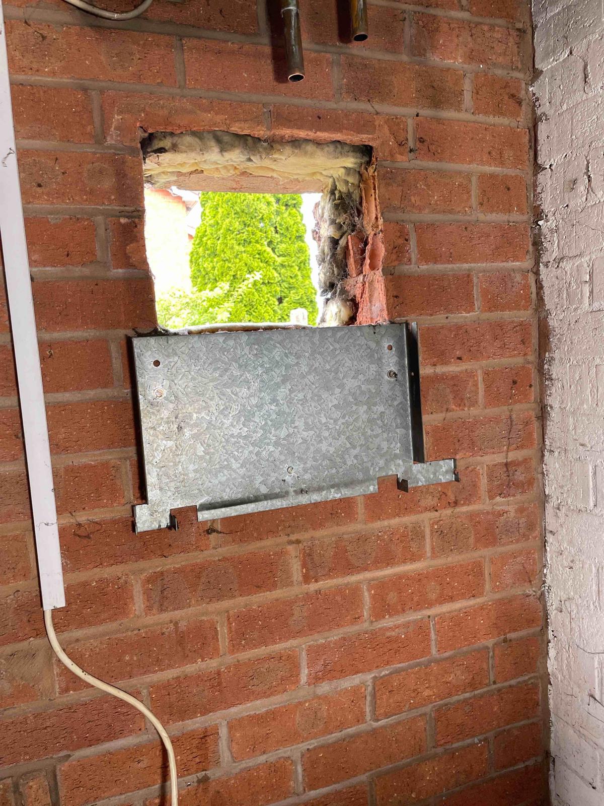Square flue opening in brick wall with metal plate before new brickwork in Walsall